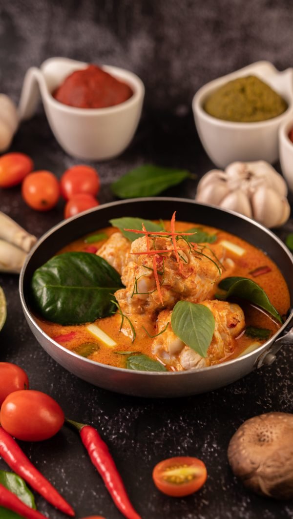 Chicken curry in a pan with lemongrass, kaffir lime leaves, tomatoes, lemon, and garlic